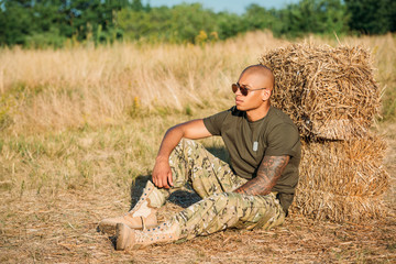 Naklejka na ściany i meble young african american soldier in military uniform and sunglasses resting near hay on range