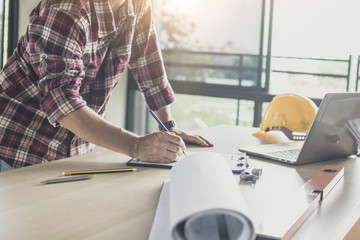 architect drawing on blueprint or engineer planning and looking on laptop