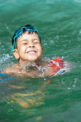 The little boy the brunette with goggles on a forehead joyfully bathes in water