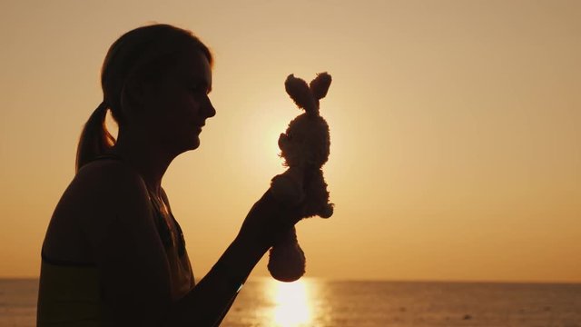 Silhouette A woman is playing with a toy bunny at dawn. Remember childhood