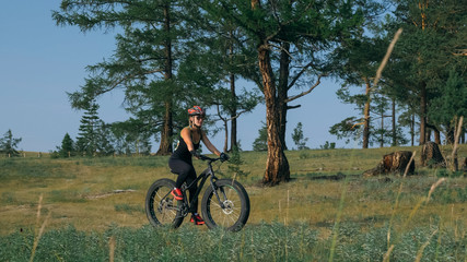 Obraz premium Fat bike also called fatbike or fat-tire bike in summer riding in the forest. Beautiful girl and her bicycle in the forest. She rolls her bike and poses to the operator.