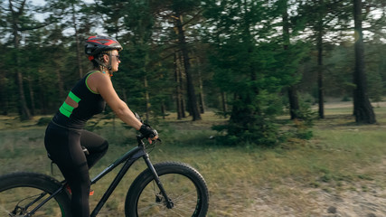 Fototapeta na wymiar Fat bike also called fatbike or fat-tire bike in summer riding in the forest. Beautiful girl and her bicycle in the forest. She rolls her bike and poses to the operator.