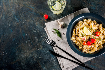 Classic italian pasta fusilli with pesto sauce, tomatoes, lime and fresh herbs in dark bowl, dark blue background  copy space top view