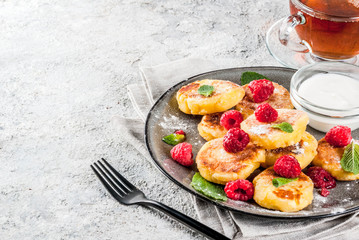 Healthy summer breakfast, cheese pancakes with raspberry, powdered sugar and mint, grey concrete background copy space