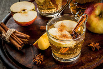 Autumn and winter drinks. Traditional home-made apple cider, cocktail of cider with aromatic spices - cinnamon and anise. On an old wooden rustic table, on a tray. Copy space