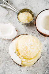 Summer healthy dessert, organic vegan coconut ice cream served in halves of coconut and ice cream cones, gray concrete background