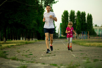 Athletic young father and little daughter running in stadium at sunset. Healthy lifestyle
