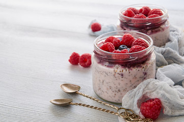 Chia milk pudding with raspberry in the glass jar with copy space for text. Decorated with fresh berries, vintage spoons and cloth. Summer detox superfoods breakfast or healthy dessert. Side view