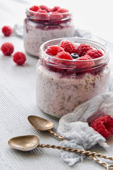 Chia milk pudding with raspberry in the glass jars decorated with fresh berries, vintage spoons on the gray kitchen background. Summer detox superfoods breakfast or healthy dessert. Side view