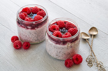 Chia pudding with raspberry in the glass jars decorated with fresh berries and vintage spoons on...