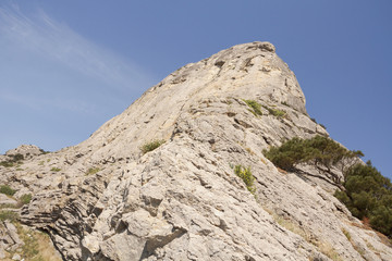 View from below on a high mountain, illuminated by the bright sun, directed into the blue sky.