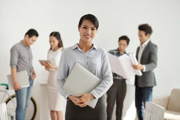 Portrait of smiling businesswomanholding folder with documents with her colleagues in the background