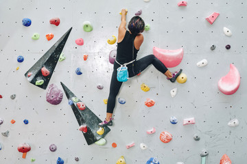Back view of woman on climbing wall with colorful artificial elements in bouldering center