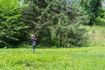 Woman photographer taking photo in a green forest in the summer.