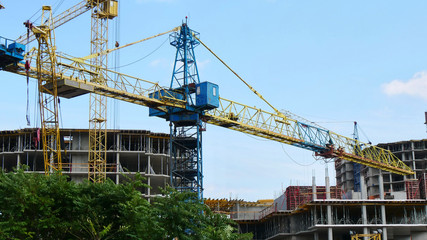 Cranes near buildings. Construction site. Concrete building under construction.