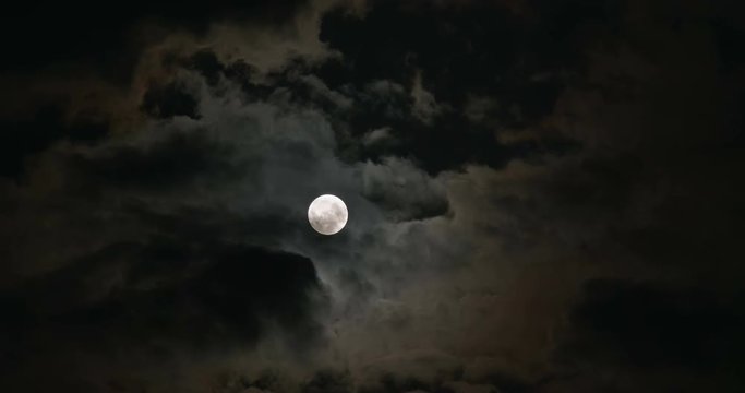 A glowing full moon in the dark and cloudy night
