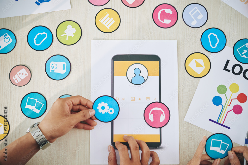 Wall mural crop shot from above of coworkers choosing set of colorful paper icons while coworking on new smartp