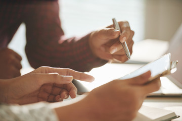 Crop close-up shot of man and woman watching tablet and discussing information at table in sunlight