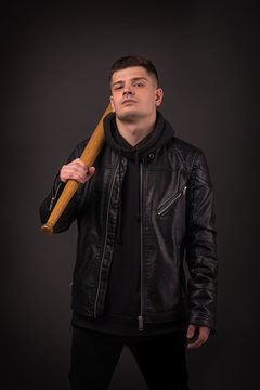 The young gue wearing leather jacket on a black wall in  fighting pose with  baseball bat