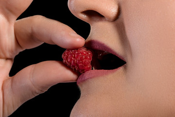 girl mouth eating raspberry on black background