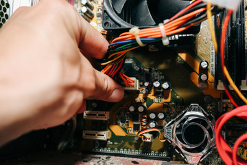 Inside details of the old personal computer. Cooler, motherboard, wires and video card in the dust. Man is holding cables in his hand. Broken PC.