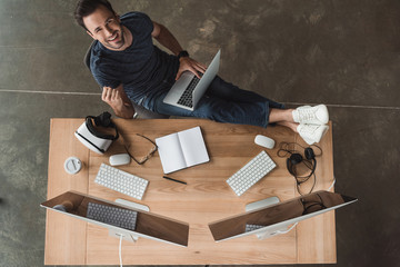 overhead view of handsome young programmer using laptop and smiling at camera