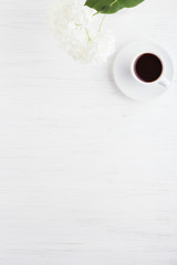 A cup of coffee and flower on white wooden table.