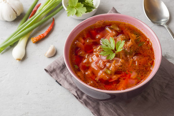 Borsch, beetroot soup in a wooden bowl with fresh herbs on a light background.