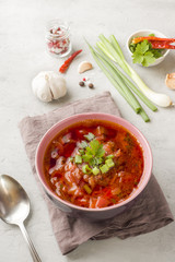 Borsch, beetroot soup in a wooden bowl with fresh herbs on a light background.