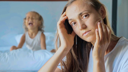 Upset mother with angry little child screaming pillow on the background