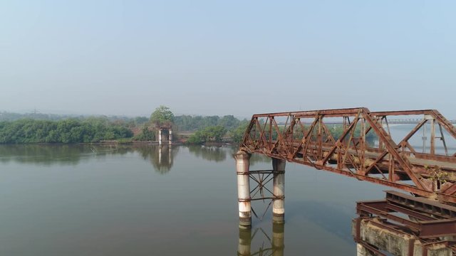 Aerial view. The camera moves over the river from shore to shore near to the remaining parts of the broken bridge. Shooting with a drone.