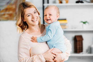 mother carrying adorable little child and looking at camera at home