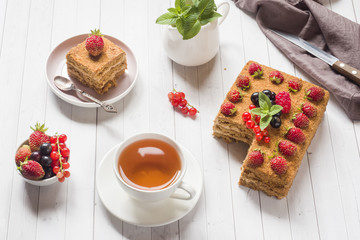 Honey cake with strawberries, mint and currant, a Cup of tea on a light background