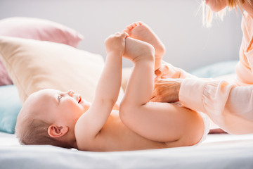 cropped shot of mother putting diaper on little child while he laughing