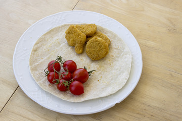 Perspective shot of chicken nuggets and small red fresh tomatoes on the wide plate as a breakfast on center