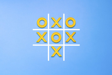 Yellow plastic crosses and a toe and a ruled field for playing tic-tac-toe on a blue background....