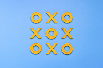 Yellow plastic crosses and zeroches for playing tic-tac-toe on a blue background. Concept XO Win...