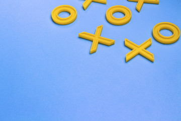 Yellow plastic crosses and zeroches for playing tic-tac-toe on a blue background. Concept XO Win...