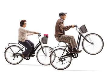 Obraz premium Elderly woman and an elderly man riding bicycles with the elderly man doing a wheelie