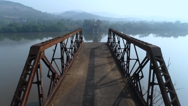 Flight from one shore to another over the big river, between the remains of the old rusty bridge truss. Shooting with a drone.