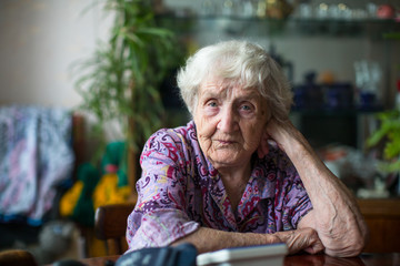 An elderly woman 85 years old sitting in a room at the table.