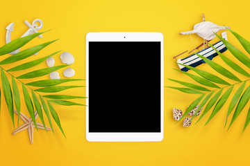 Palm leaves, seashells, boat, starfish, anchor and tablet with empty screen on yellow background. Empty space. Travel concept. Summer holiday background. Flat lay. Mock-up
