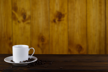 White cup and coffee beans on a brown wooden table.