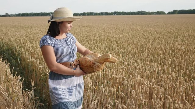 A young woman carries a basket of freshly baked bread, walking along a ripe wheat field. Slow motion steadicam shot