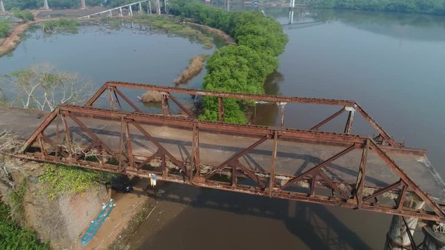 Aerial view. Flying around of supports old, rusty, dilapidated bridge over the river. Shooting with a drone.