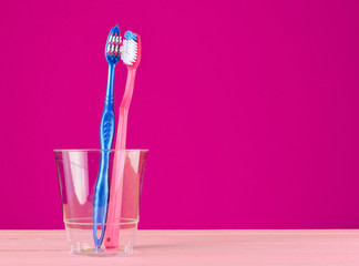 Two toothbrushes in a transparent plastic cup in the bathroom on pink background, copy space,...