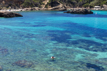 beautiful landscape in Ibiza of blue ocean in a sunny day with a woman floating on a flatable donuts. Summer and holidays concept.