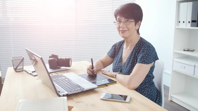 Graphic designer aged woman using digital graphic tablet while working at modern office