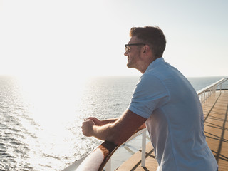 Fototapeta na wymiar Stylish, young man in sunglasses on the deck of a cruise ship, looking into the distance against the background of the morning sunrise and the blue sky. Concept of sea travel and recreation