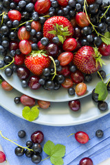 Fruit salad with strawberry, blueberry, cherry, gooseberry and black currant on wooden gray background. Flat lay. Top view